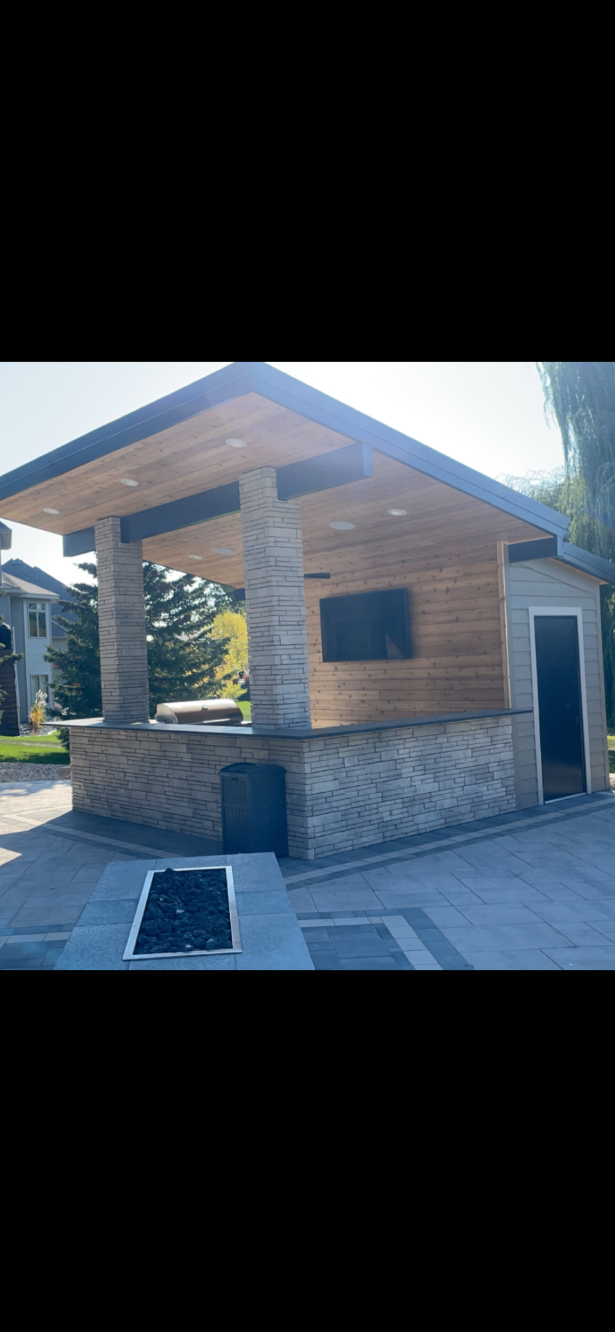 Modern outdoor covered kitchen with stone columns, built-in TV and paver patio