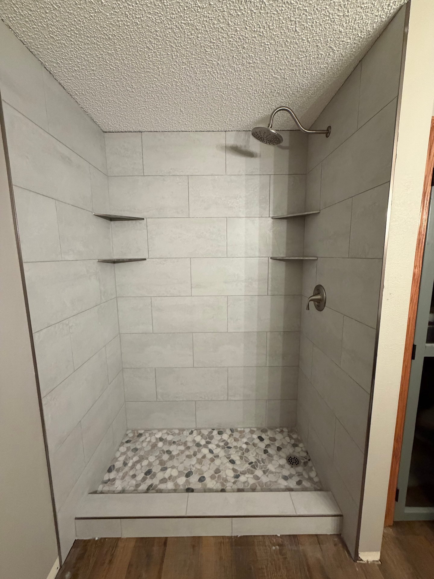 Walk-in tiled shower with pebble mosaic floor and corner shelves